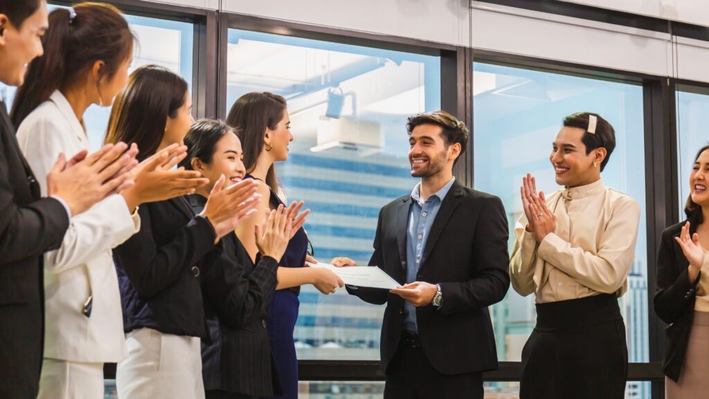 A group applauds as a man receives a DILIsym award in office, highlighting 2024's successes.