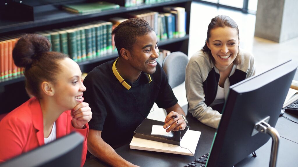 Three people study ESG data on a monitor using Simulations Plus software in a library setting.